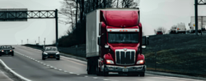 A red delivery truck on a highway under an overhead sign gantry